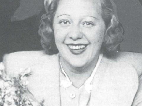 Black and white photograph of Gwlady Stanley smiling at the camera while holding flowers